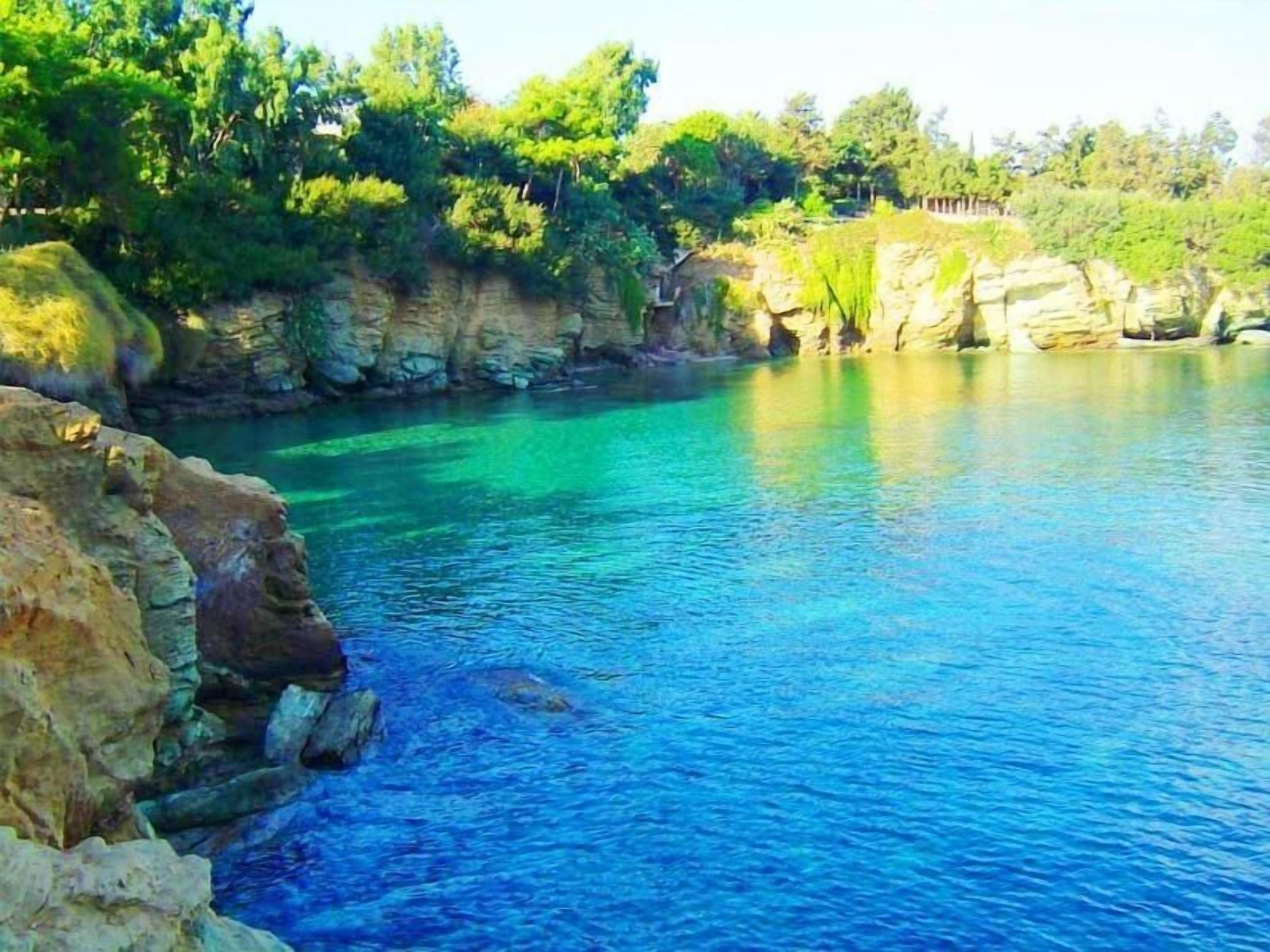 A clear blue body of water surrounded by rocky cliffs and dense greenery.