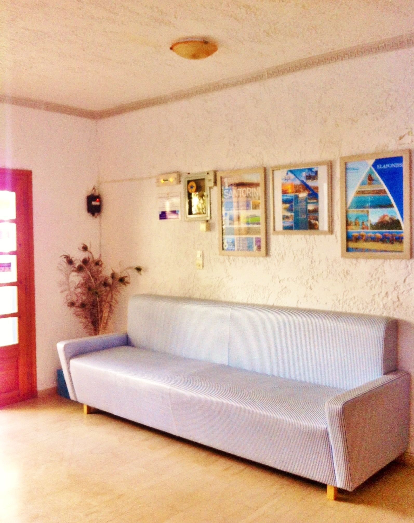 Quarto com sofá azul claro, piso de madeira e parede branca com textura e quadros emoldurados.