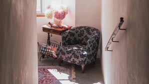 A narrow hallway with a floral arrangement on a table, a patterned armchair, and a small table with a vase and a book. - Hotel Traube (Bressanone)