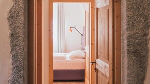 A narrow hallway leading to a bedroom with a bed, a lamp, and wooden doors. - Hotel Traube (Bressanone)