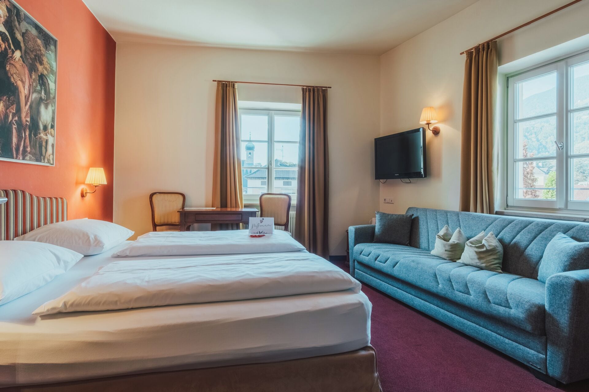 A hotel room with a bed, a sofa, a desk, and a TV.