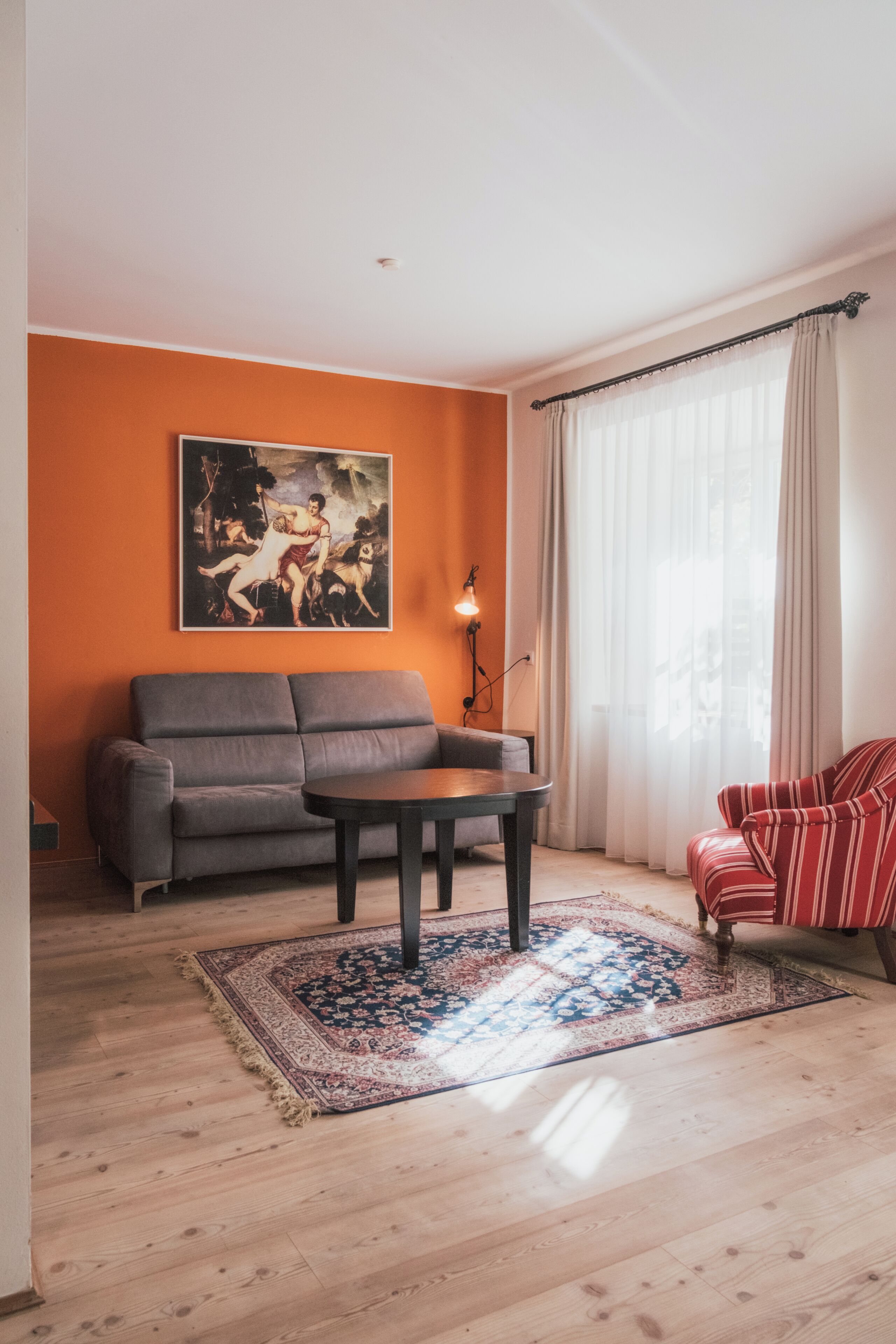 A living room with a sofa, a table, a rug, a painting, and a window with curtains.
