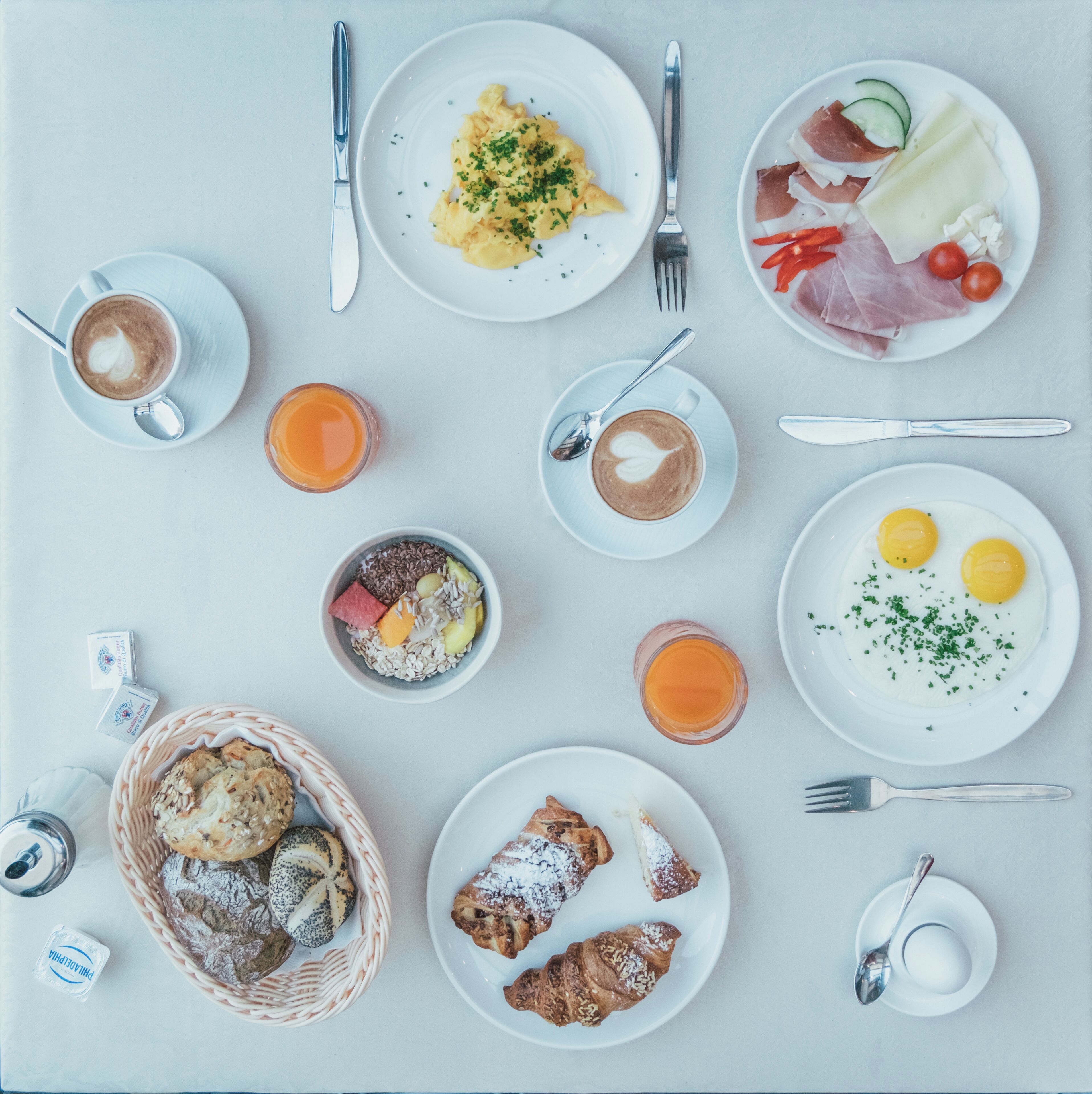 Une table dressée pour le petit-déjeuner, avec des assiettes d’œufs, des toasts et des viennoiseries, ainsi que du café et du jus de fruits.