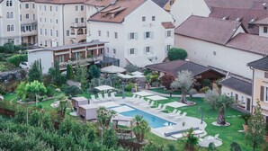 A hotel courtyard with a swimming pool, lounge chairs, and a bar area. - Hotel Traube (Bressanone)