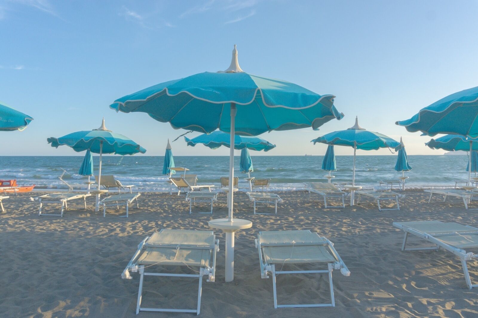 Una spiaggia con diversi ombrelloni azzurri e lettini bianchi disposti sulla sabbia.