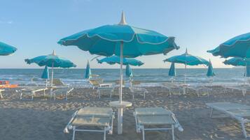 Una spiaggia con diversi ombrelloni azzurri e lettini bianchi disposti sulla sabbia.