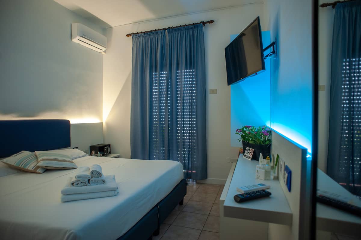 Habitación de hotel con cama, escritorio con computadora, televisor montado en la pared y ventana con cortinas.