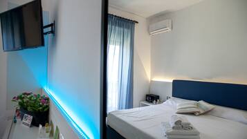 Una camera d'albergo con un letto, una TV a schermo piatto montata a parete, un comodino con una lampada e una finestra con tende.