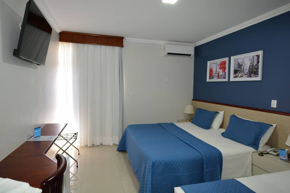 A hotel room with two beds, a desk, a chair, a TV, and two framed pictures on the wall.