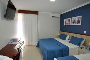 Una camera d'albergo con due letti, una scrivania, una sedia, un televisore e due quadri appesi al muro.