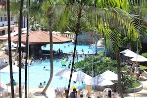 A swimming pool area with multiple people, palm trees, and umbrellas. - Taiyo Thermas Hotel (Caldas Novas)