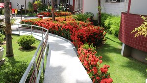 A courtyard with a curved walkway, surrounded by red flowers and green plants. - Taiyo Thermas Hotel (Caldas Novas)