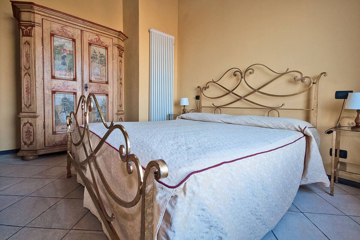 A bedroom with a metal bed frame, a large wooden cabinet with artwork, and a radiator.