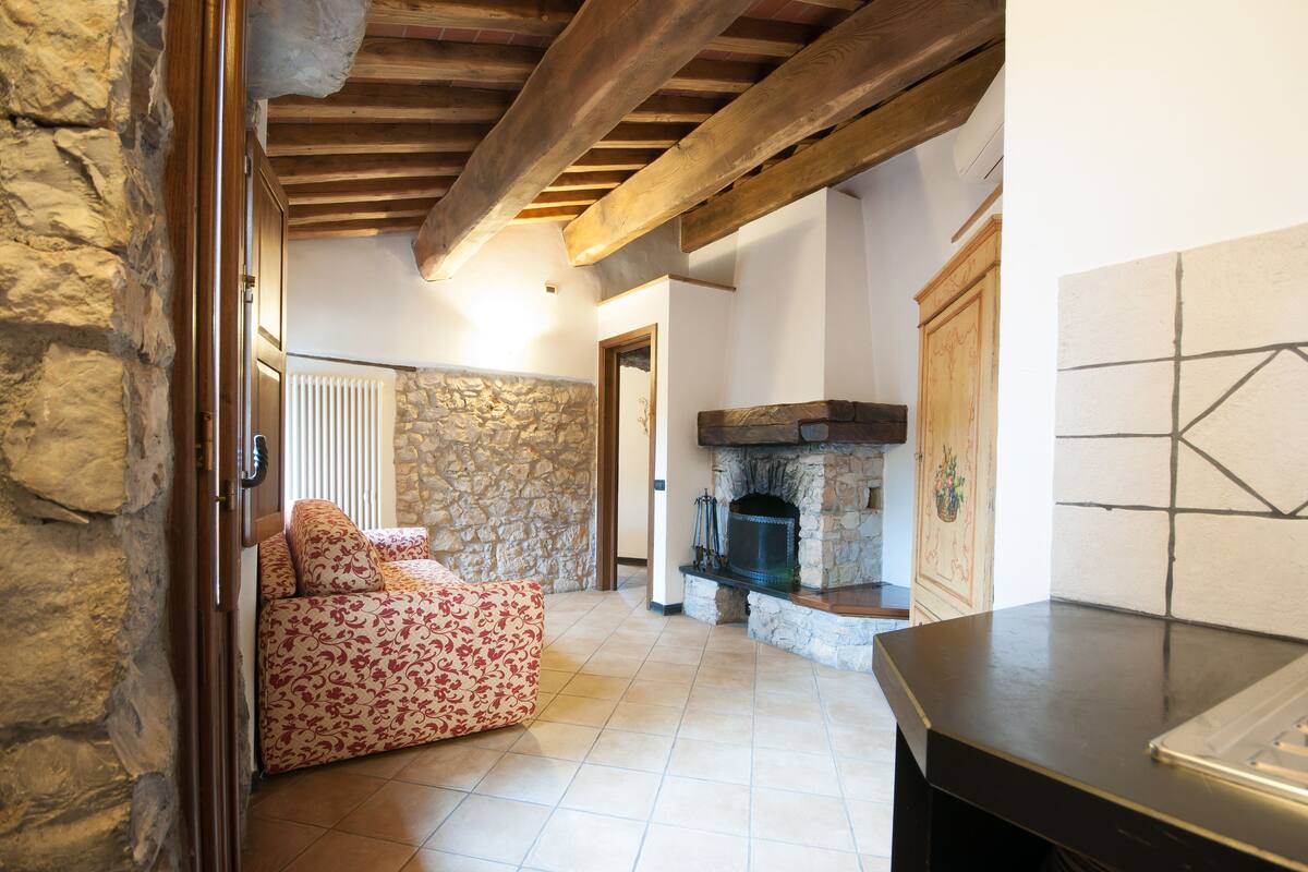 A cozy living room with a stone wall, wooden beams, a fireplace, and a patterned sofa.