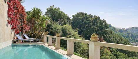 Una piscina con vista a exuberante vegetación y edificios a lo lejos.