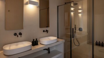 Un baño moderno con dos lavamanos blancos, un espejo grande y una zona de ducha con paredes de vidrio.
