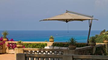 A patio with a view of the ocean, potted plants, and a large umbrella.