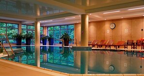An indoor swimming pool with a clear view of the outside through large windows, a clock on the wall, and several lounge chairs along the poolside. - Hotel Dwór Elizy blisko Sky Bridge (Bystrzyca Klodzka)