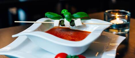 A white ceramic dish with a red sauce, a skewer with mozzarella and basil, and a glass candle on a table.