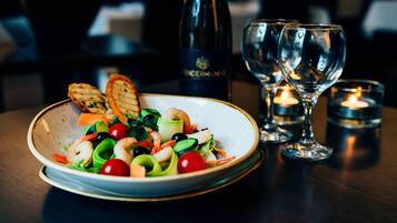 Un piatto di insalata di gamberi e verdure, una bottiglia di vino e due bicchieri da vino su un tavolo con candele.