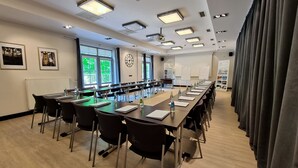 A conference room with long tables, chairs, and a large window with curtains.