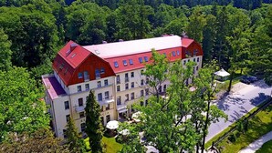 A large, multi-story building with a red roof, surrounded by lush greenery and trees.