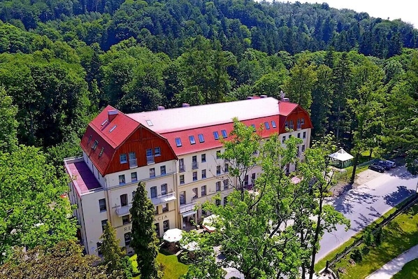 A large, multi-story building with a red roof, surrounded by lush greenery and trees.