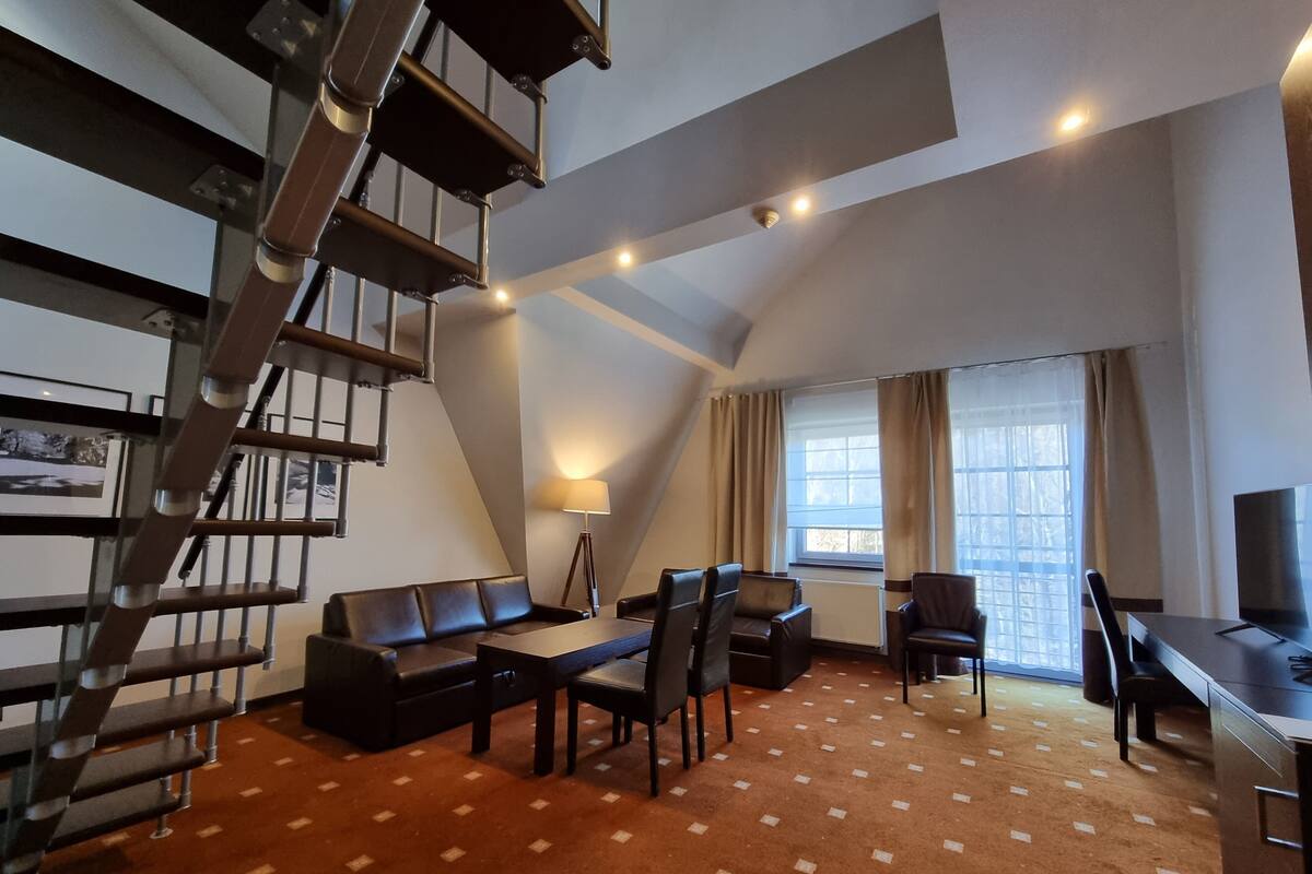 Un salon moderne comprenant un canapé, des fauteuils, une table à manger et un téléviseur. On y trouve également un escalier et une fenêtre avec des rideaux.