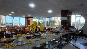 Disposição de buffet com diversos alimentos e uma ampla vista pela janela.