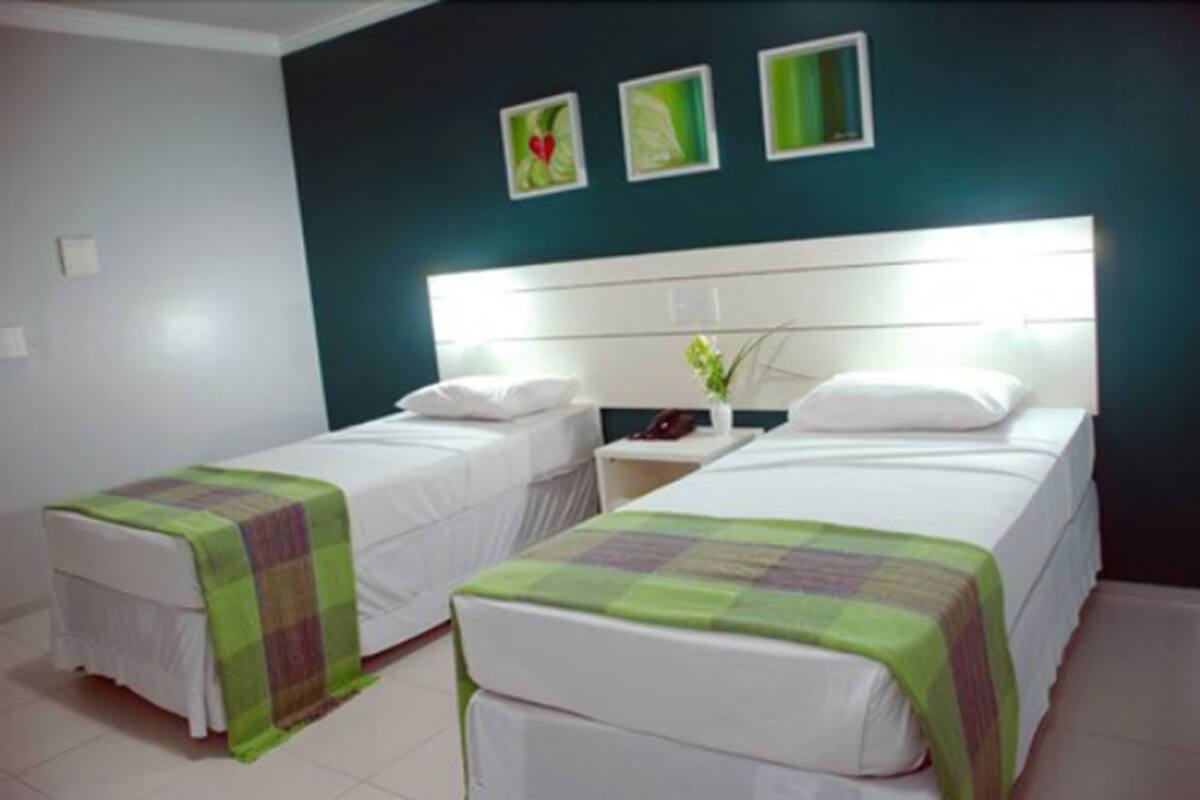 Habitación de hotel con dos camas, una mesita de noche con lámpara y una pared decorada con tres cuadros enmarcados.