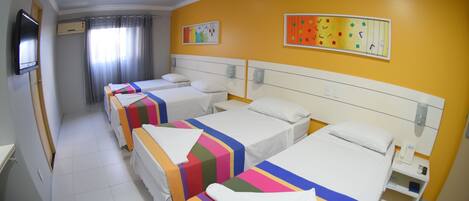 A hotel room with three beds, each with colorful bedding, a flat-screen TV, and artwork on the walls.