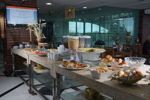 Una mesa de buffet con diversos alimentos y recipientes, una planta en maceta, y un cartel en la pared.