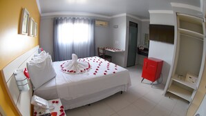 Quarto de hotel com cama, escrivaninha, guarda-roupa e banheiro.
