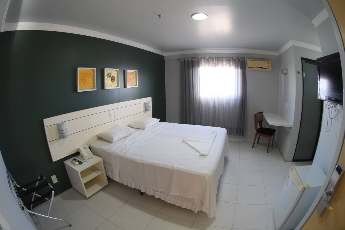 Una habitación de hotel con una cama grande, un escritorio, una silla, un televisor y obras de arte en la pared.