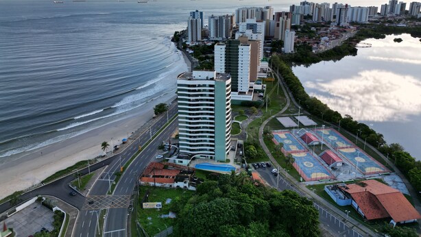 Paisagem costeira com edifícios altos, uma praia e um complexo desportivo.