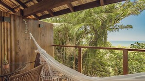 Una terraza de madera con una hamaca, una silla de mimbre y una planta en maceta.