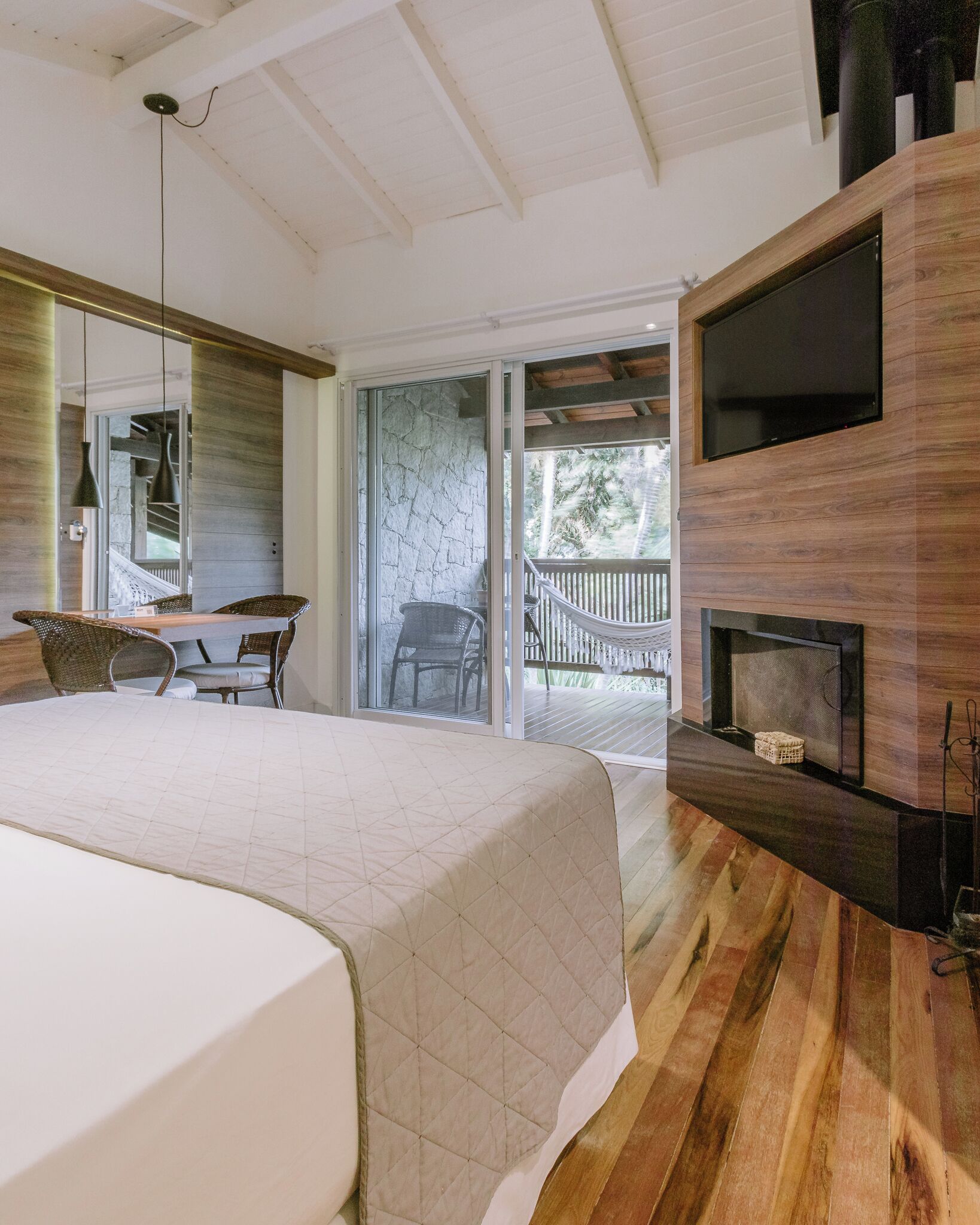A modern bedroom with a large bed, a TV mounted on the wall, and a fireplace.