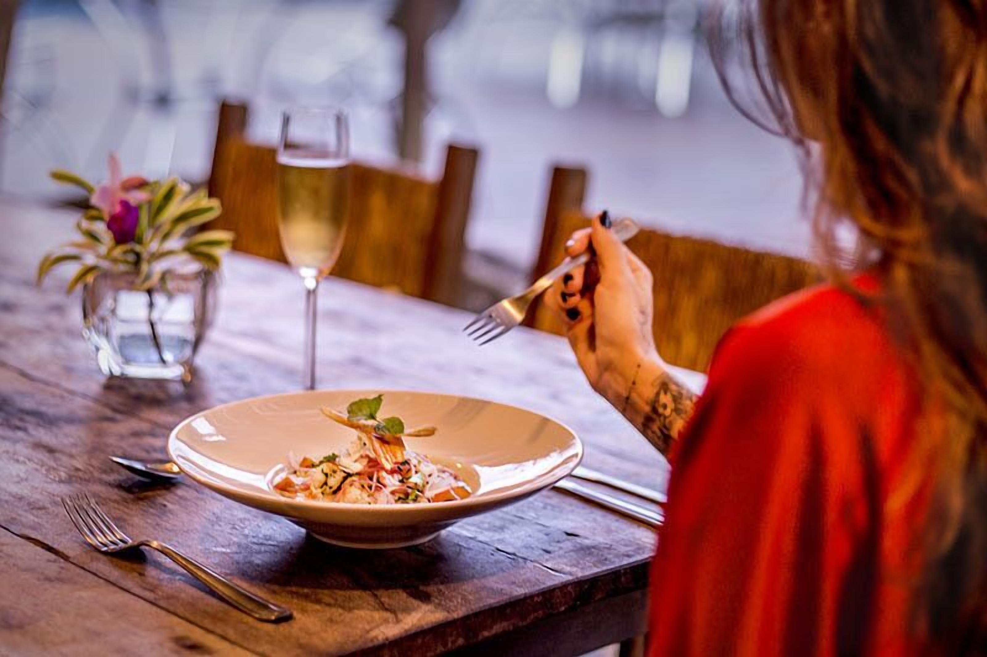 Una mesa de comedor con un plato de comida, una copa de vino y un jarrón pequeño con flores.