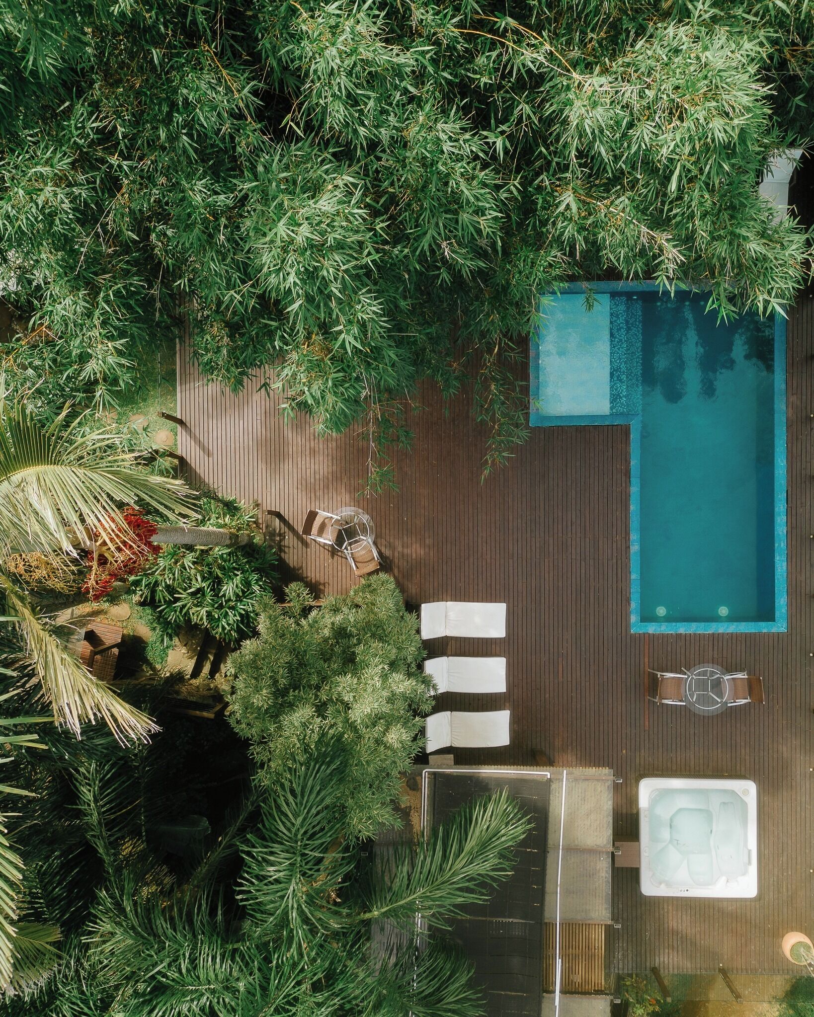 An aerial view of a backyard with a swimming pool, wooden deck, and outdoor seating area surrounded by lush greenery.