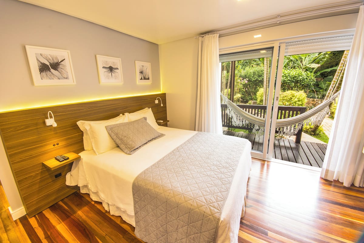 A bedroom with a large bed, wooden headboard, bedside tables, and a view of a balcony with a hammock.