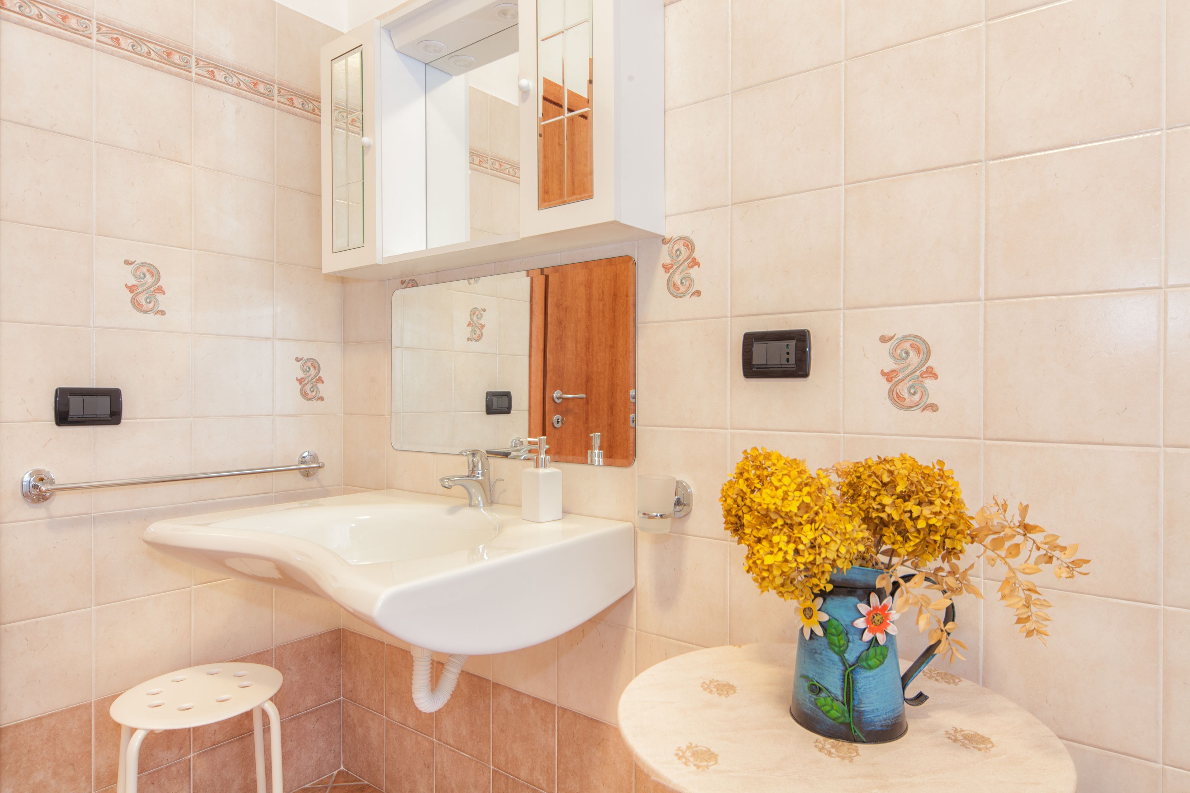 A bathroom with a sink, mirror, and a vase with flowers on a round table.