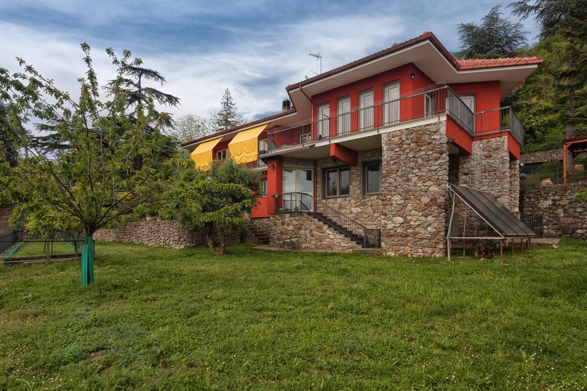 Una casa de dos pisos con base de piedra, fachada roja y amarilla, y un balcón.