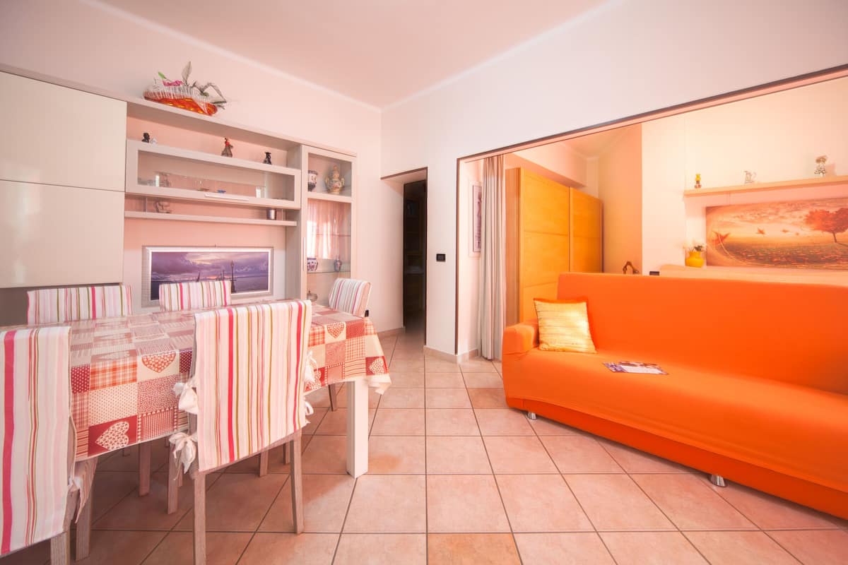 Una sala de estar con una mesa de comedor, sofá naranja y televisor en la pared.