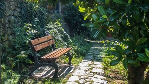 A stone pathway leading to a wooden bench surrounded by lush greenery and a stone wall. - Oasi Verde (Castiglione Chiavarese)