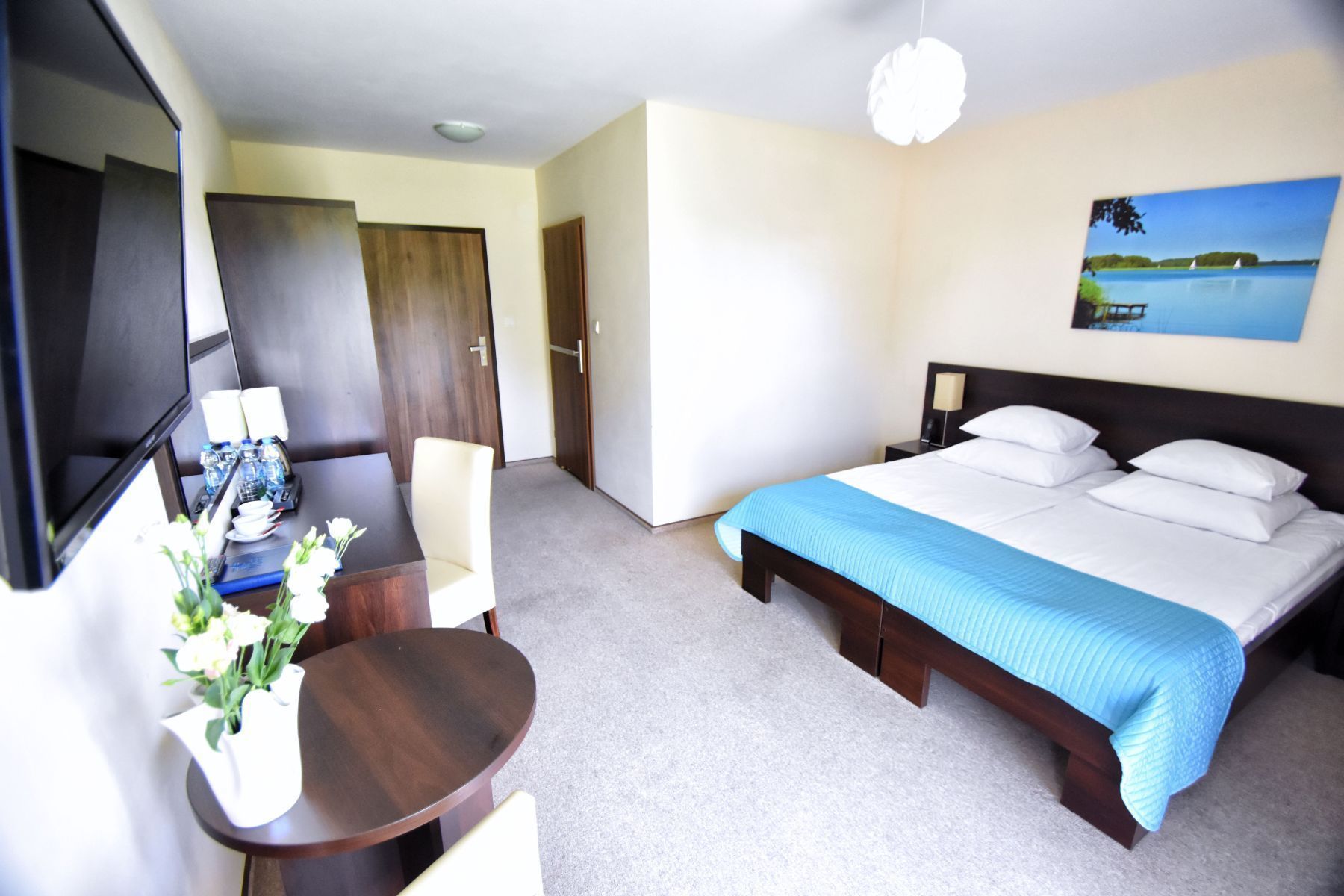 A hotel room with a bed, a desk with a chair, a TV, and a painting on the wall.