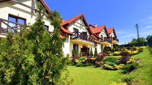 A row of traditional-style houses with red roofs and balconies, surrounded by well-maintained gardens and greenery. - Hotel Santa Monica (Mikolajki)