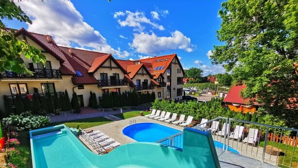 A swimming pool with a slide, surrounded by lounge chairs and a garden. - Hotel Santa Monica (Mikolajki)