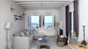 Ett vardagsrum med en soffa, ett soffbord och två fönster med utsikt över havet.