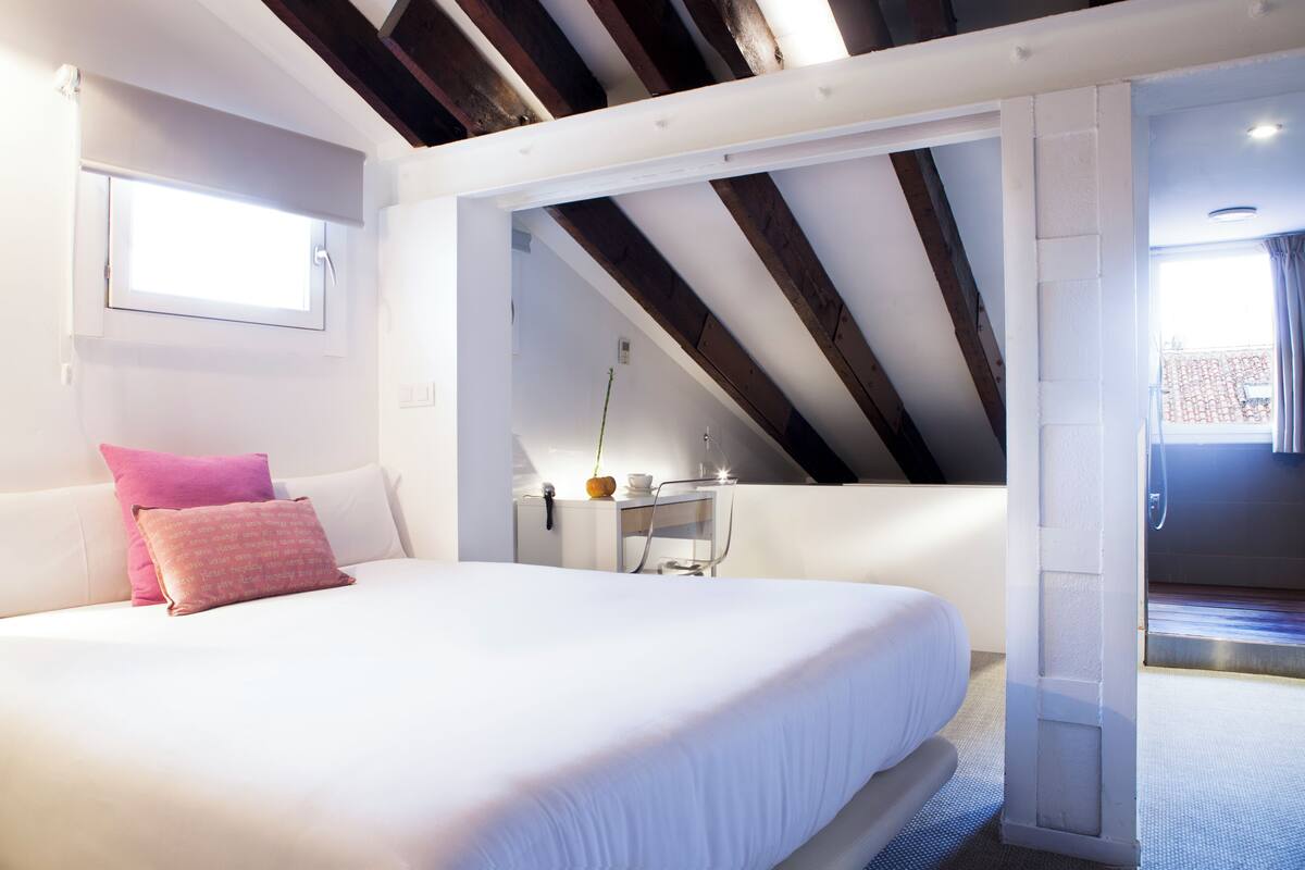 A bedroom with a large bed, a window, a skylight, and a view of the outside.