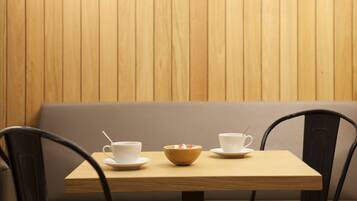 Une table en bois, sur laquelle sont posées deux tasses blanches et un bol, le tout placé devant un mur en bois.